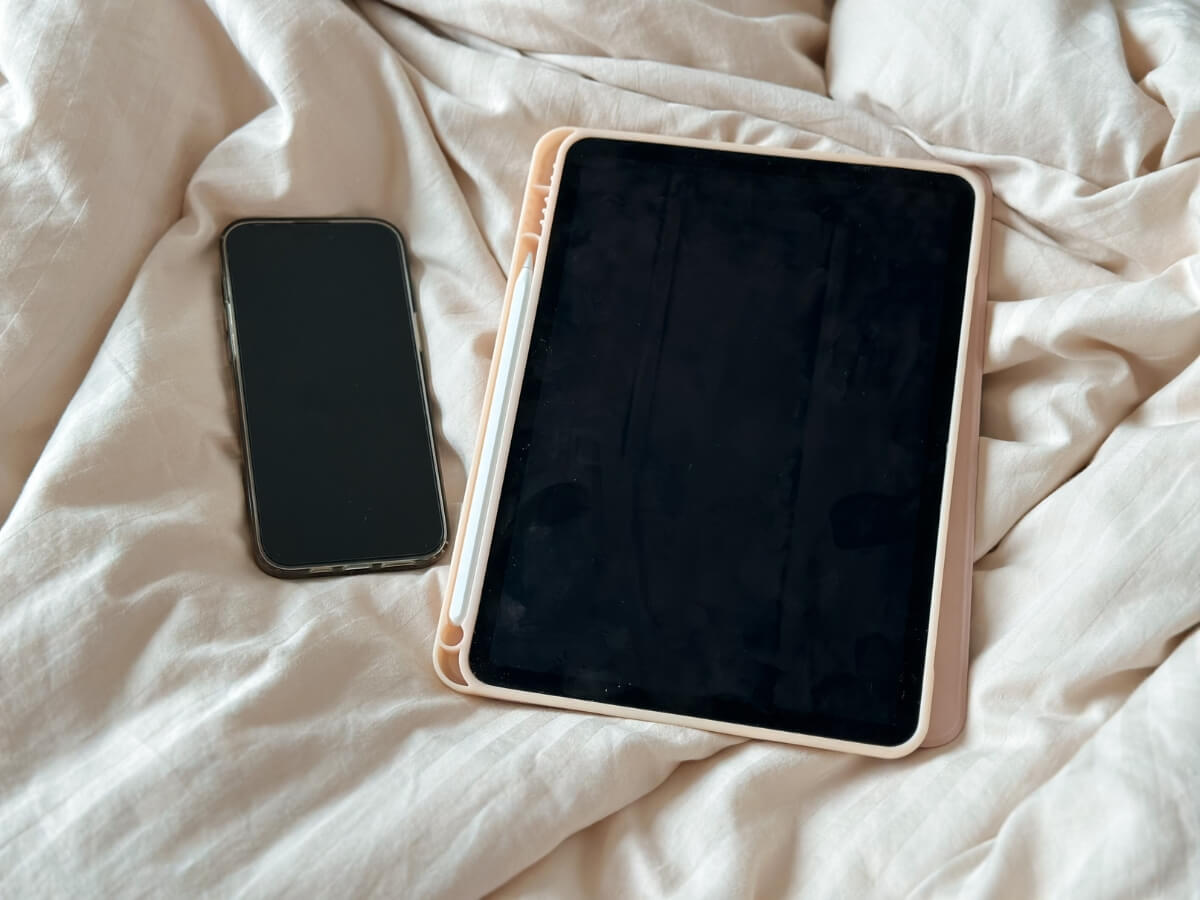 Vypnutý Smartfón a tablet položené na posteli.