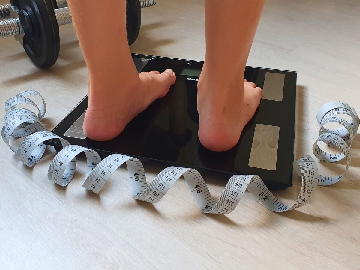 Človek na osobnej váhe a krajčírsky meter.